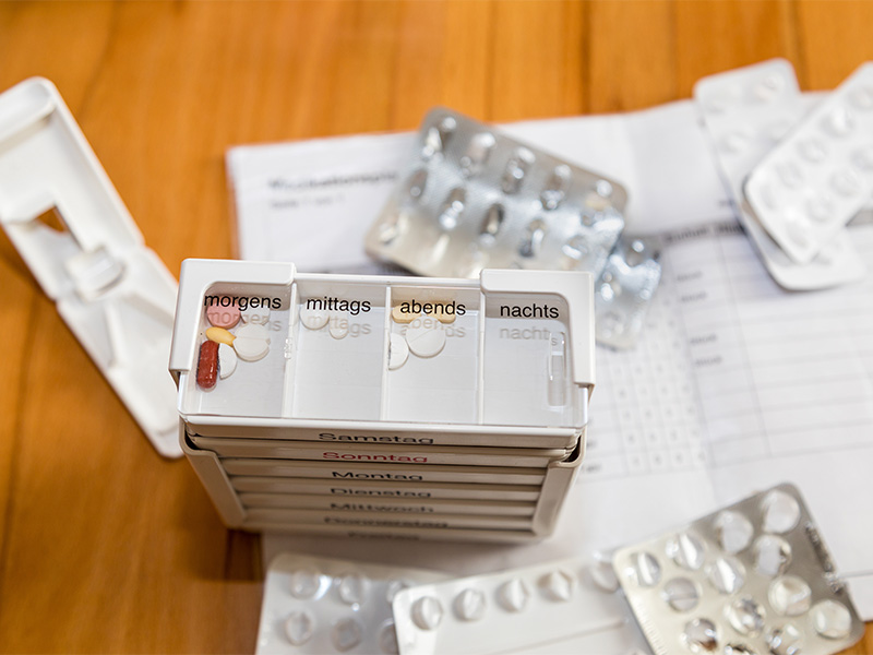 Pflegekraft bereitet Medikamente übersichtlich nach Wochentagen und Einnahmezeiten für eine sichere häusliche Versorgung eines Patienten vor.