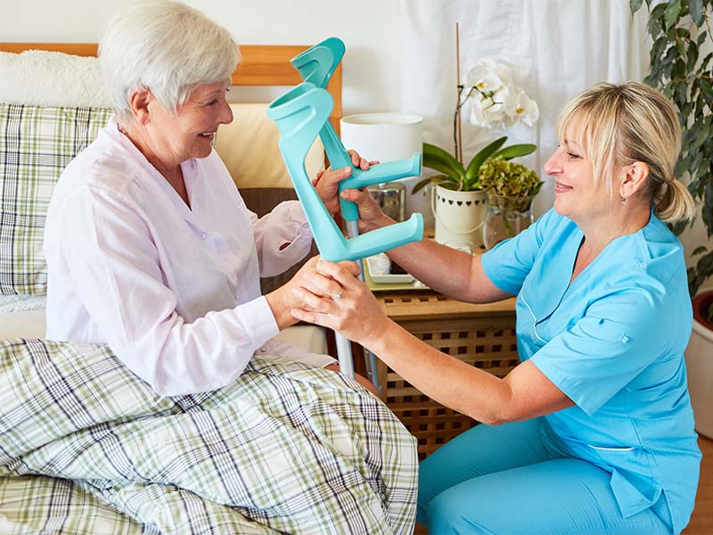 Altenpflegerin hilft einer Seniorin beim Aufstehen mit Krücken