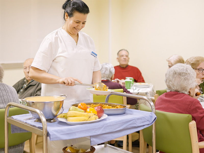 Koch serviert Seniorinnen und Senioren in einem Pflegeheim eine Mahlzeit und sorgt für Genuss und gemeinsame Zeit.
